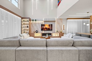 A modern living room with a large sectional sofa, a flat-screen TV, and a fireplace.