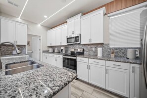 Eine moderne Küche mit weißen Schränken, Granit-Arbeitsplatten, Edelstahlgeräten und einer Spritzschutzwand.