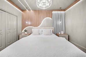 A bedroom with a large bed, wooden paneling, a chandelier, and a nightstand with a plant.