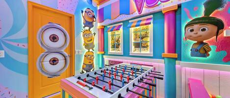 A colorful room with a foosball table, a door with a circular window, and a wall with a Minion character.