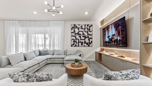 A modern living room with a sectional sofa, a round coffee table, and a flat-screen TV mounted on the wall.