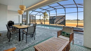 A poolside area with a wooden table and chairs, a lounge chair, and a view of the pool and landscape.