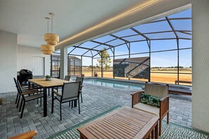 Uma área à beira da piscina com mesa e cadeiras de madeira, uma espreguiçadeira e vista para a piscina e paisagem.