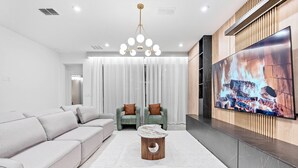 A modern living room with a sectional sofa, two armchairs, a coffee table, and a flat-screen TV displaying a fireplace.