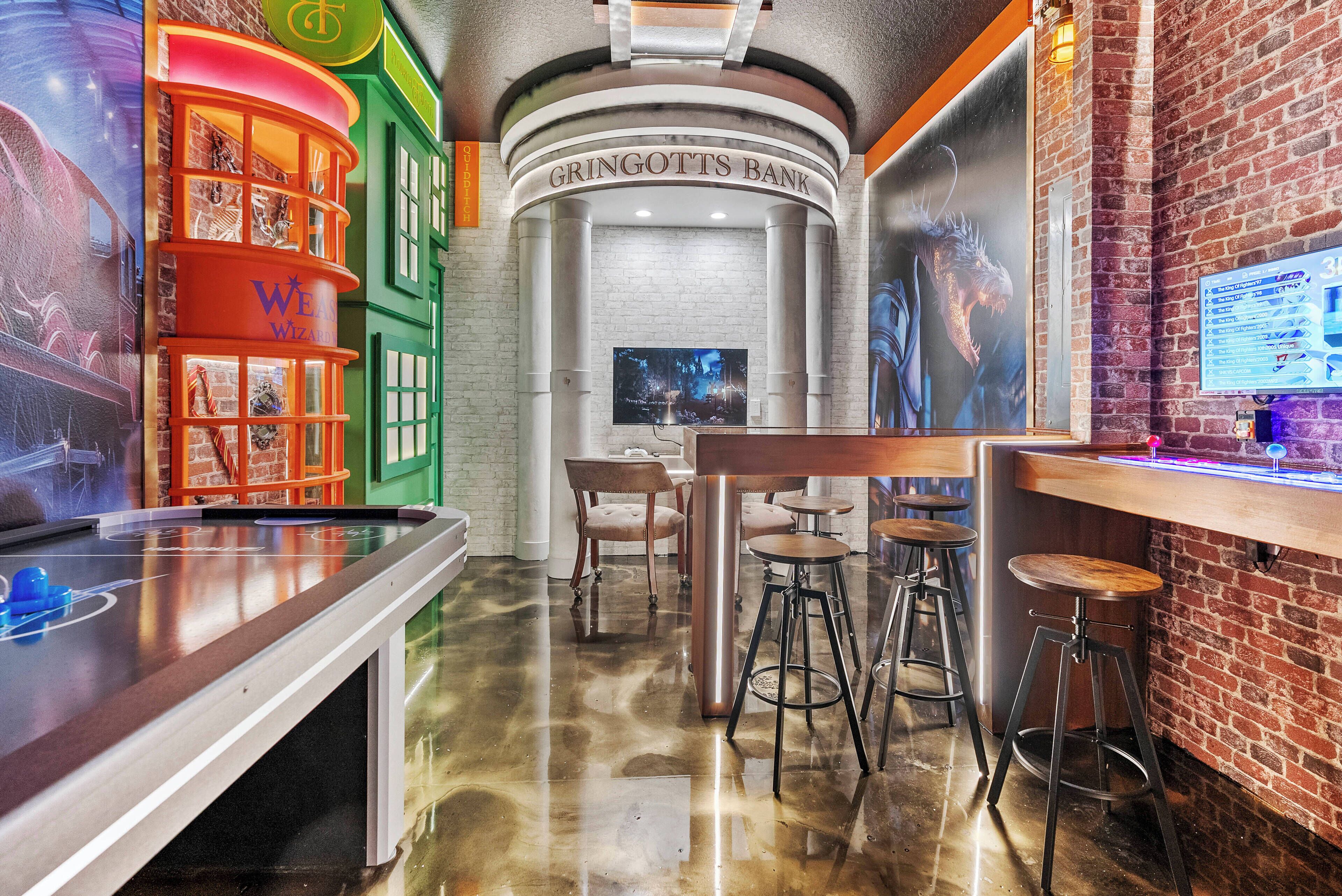 A bar area with a pool table, stools, and a television screen.