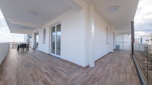 A spacious balcony with a wooden floor, a dining area, and a sliding glass door. - Apartment 'Grace Home 1' with Sea View, Wi-Fi and Air Conditioning (Milazzo)