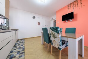 Una cocina moderna con estufa integrada, una zona de comedor con dos sillas, un televisor montado en la pared y un tapete estampado en el suelo.