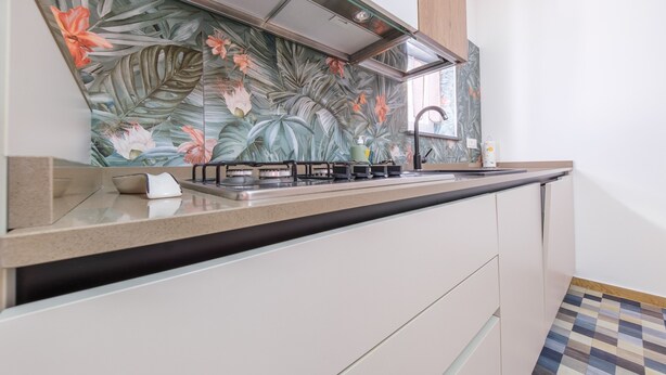 A kitchen with a modern design, featuring a stainless steel range hood, a countertop with a sink, and a backsplash with a tropical leaf and flower pattern. - Apartment 'Grace Home 1' with Sea View, Wi-Fi and Air Conditioning (Milazzo)