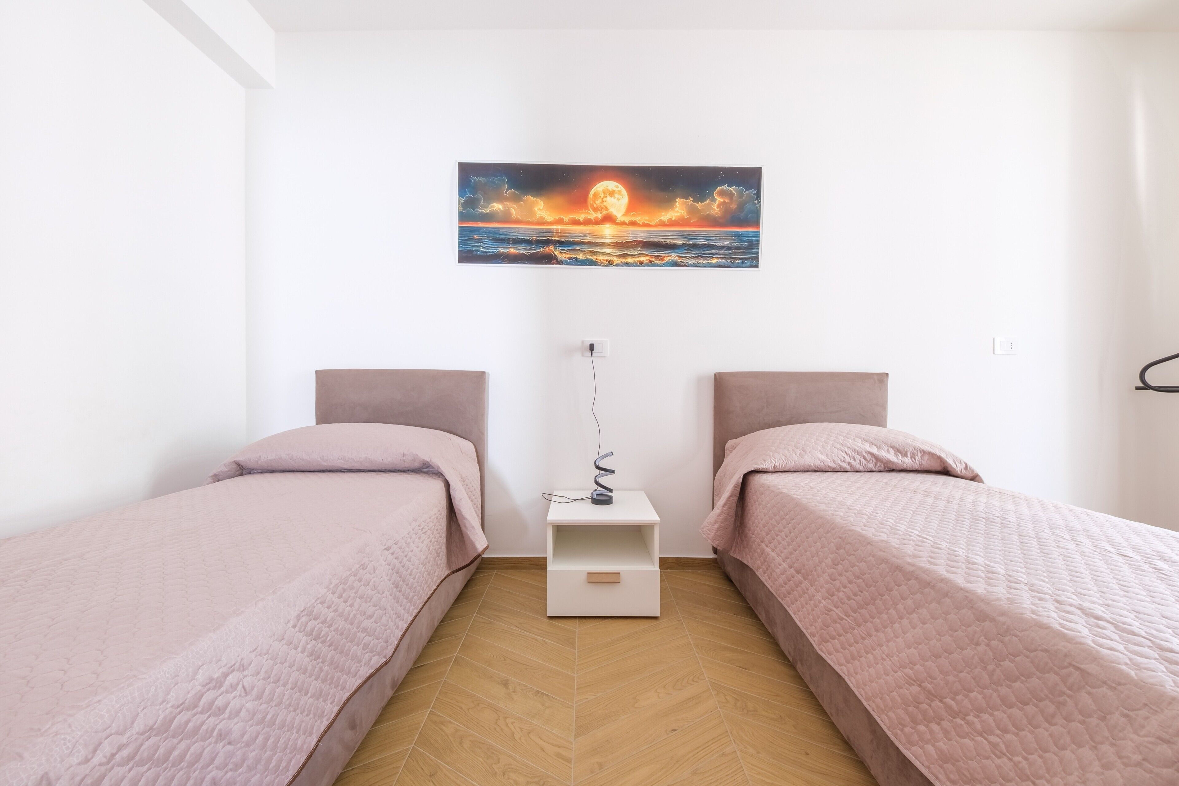 Une chambre avec deux lits, une table de chevet, un tableau accroché au mur et un plancher en bois.