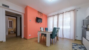 A dining area with a table and chairs, a television mounted on the wall, and a kitchen area with appliances. - Apartment 'Grace Home 1' with Sea View, Wi-Fi and Air Conditioning (Milazzo)