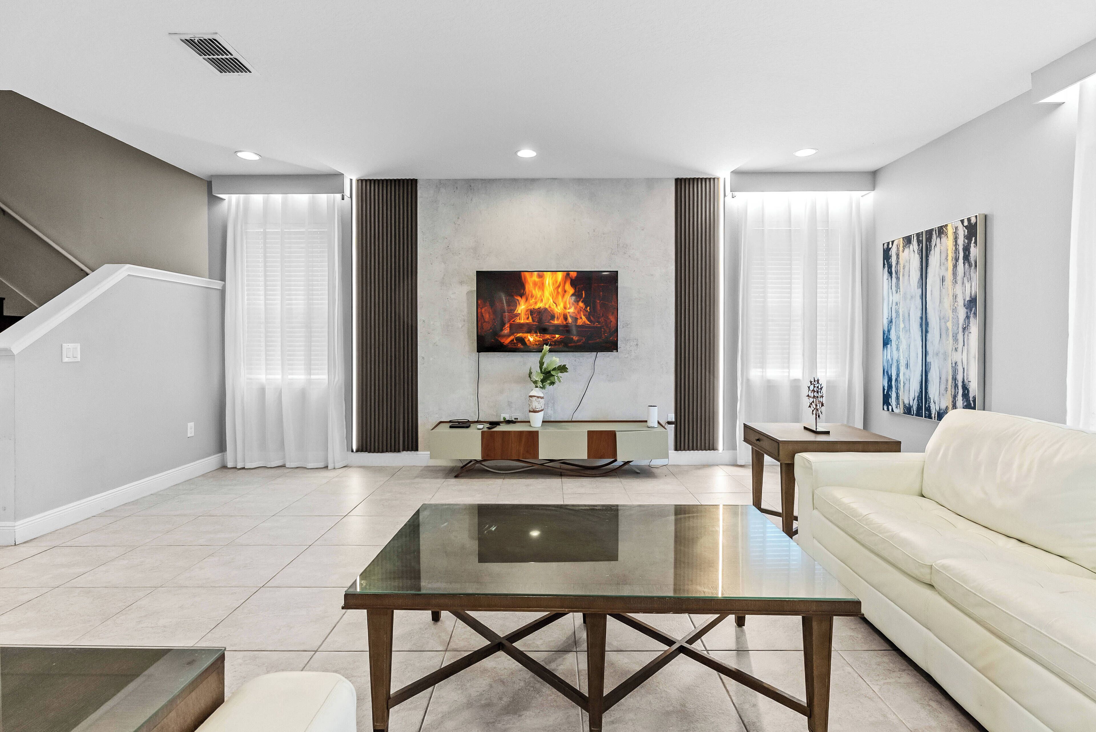 Unwind in the spacious living area featuring a comfy cream sofa and a chic glass coffee table. Enjoy the natural light streaming through sheer curtains, illuminating modern artwork and a sleek TV setup for your entertainment.