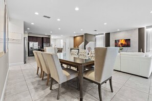 Join us at the chic dining table, where plush chairs invite conversation. Enjoy the bright, airy space with sleek tile floors, flowing effortlessly into a cozy living area adorned with modern decor for a perfect gathering.