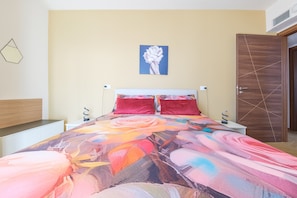 Une chambre à coucher avec un lit, deux oreillers rouges, une table de chevet, une horloge murale, un tableau et une armoire en bois.