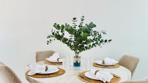 Une table de salle à manger ronde, surmontée d’un plateau en marbre, est entourée de quatre chaises en velours aux pieds noirs. Une petite plante est placée au centre de la table.