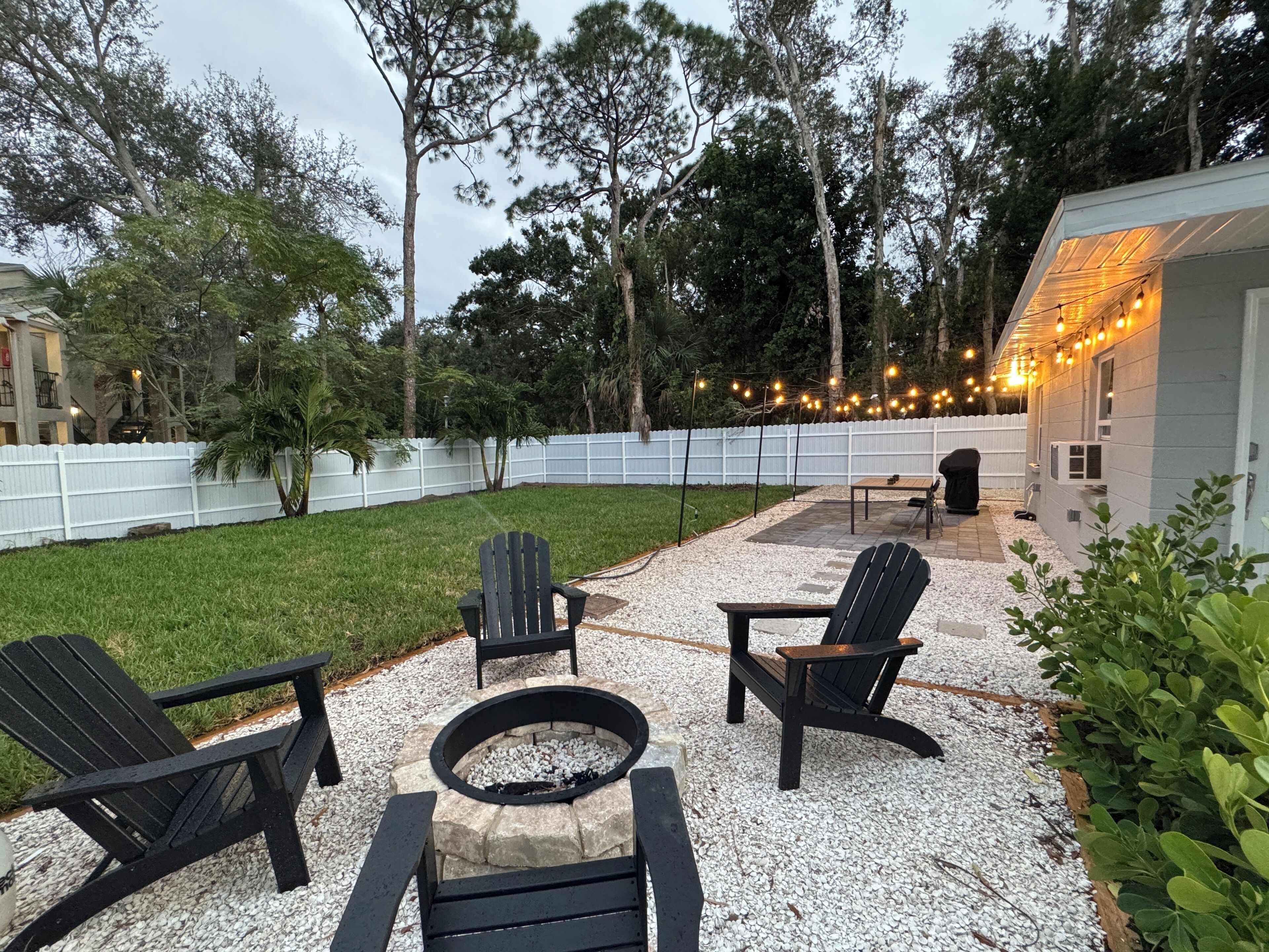 Un jardin avec un foyer, deux fauteuils Adirondack et une table.