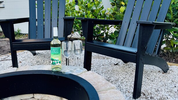 Une terrasse avec deux fauteuils Adirondack, un foyer et une bouteille de vodka de la marque Sunset.