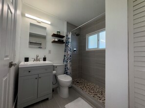 Et badeværelse med toilet, vask, underskab, brusebad og et vindue.