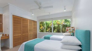 Une chambre avec deux lits, un bureau, une armoire et une fenêtre donnant sur un espace verdoyant.