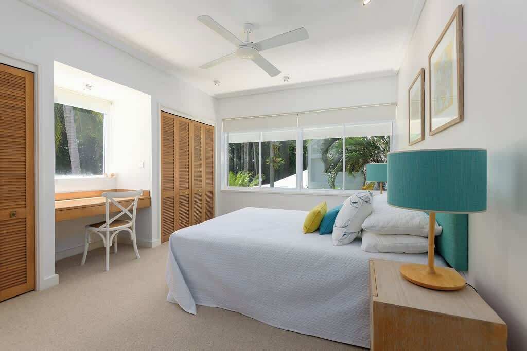 Une chambre à coucher comprenant un lit, un bureau, une chaise, un ventilateur de plafond et une fenêtre donnant sur un paysage verdoyant.