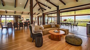 A spacious living area with a wooden floor, a sofa, a coffee table, and a dining area with chairs and a table. - Bangalow - Best View in Port Douglas (Port Douglas)