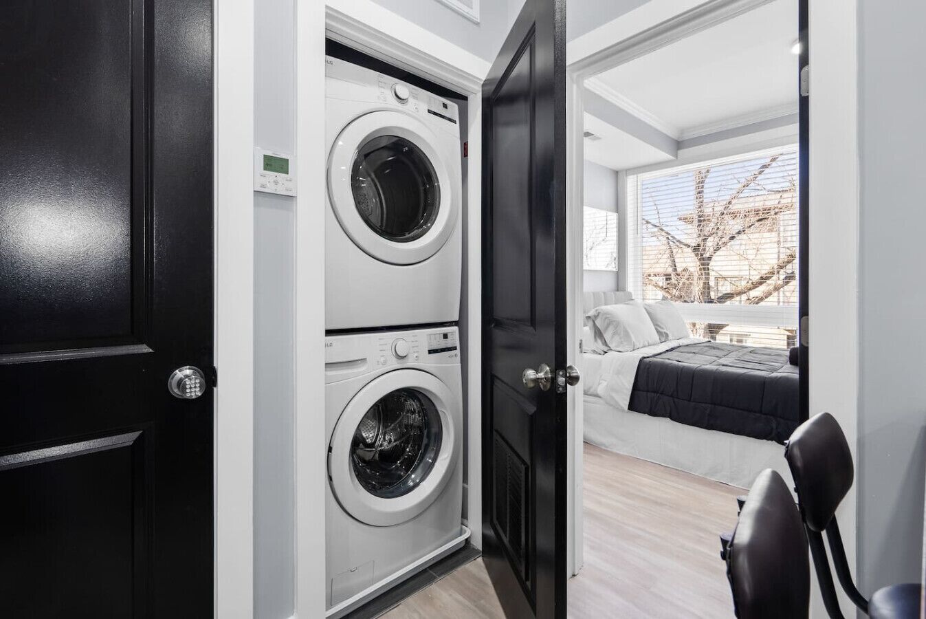 Apartamento moderno com porta preta que dá acesso a uma lavanderia com duas máquinas de lavar LG.