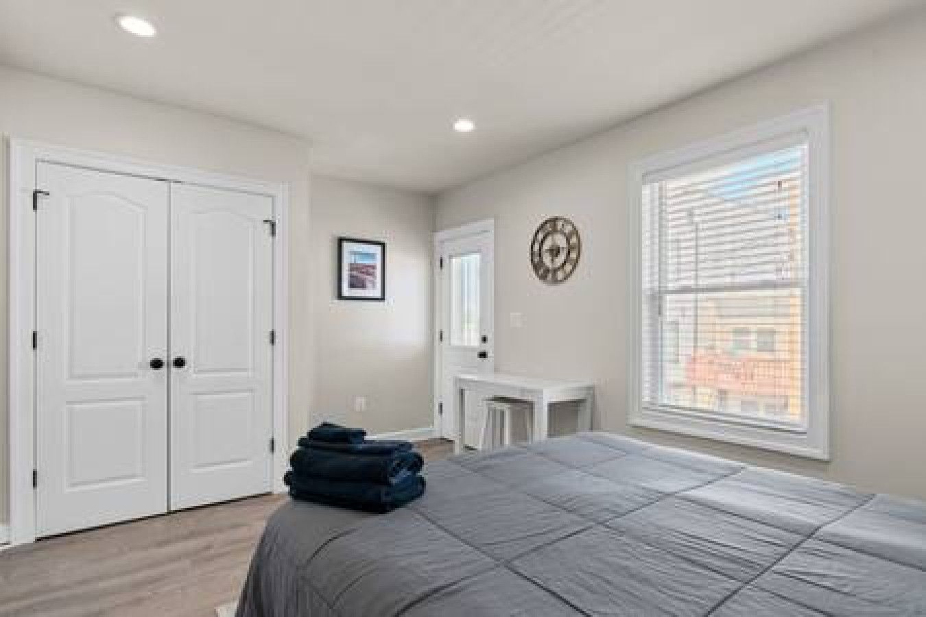 A bedroom with a bed, a desk, a chair, a wardrobe, and a window with blinds.