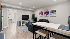 A modern living room with a flat-screen TV, a dining table, and a sofa. - Chic Condo +Heart Of DC+Steps From Attractions (Washington)