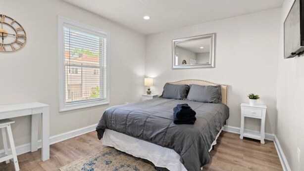 A bedroom with a bed, bedside tables, a mirror, and a window with blinds. - Chic Condo +Heart Of DC+Steps From Attractions (Washington)