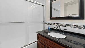 A modern bathroom with a white shower enclosure, a black sink with a single faucet, and a mirror above the sink. - Chic Condo +Heart Of DC+Steps From Attractions (Washington)