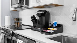 Une cuisine moderne équipée d’une cuisinière intégrée, d’un four à micro-ondes et d’une machine à café. On y trouve des couteaux, une boîte à thé et une machine à café sur le plan de travail.