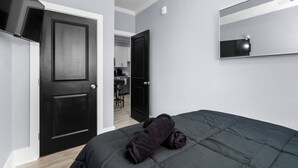 Une chambre à coucher avec un lit, une porte sombre, un miroir et une vue sur la cuisine.