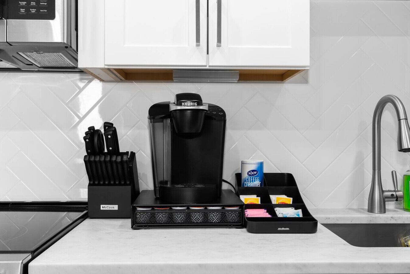 A modern kitchen with a Keurig coffee maker, a coffee creamer dispenser, and a knife block.