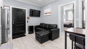 Un salon moderne avec un canapé en cuir noir, un téléviseur à écran plat et un coin repas comprenant une table et des chaises en bois.