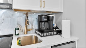 A kitchen with a stainless steel sink, a coffee maker, a hand soap dispenser, and a paper towel holder.
