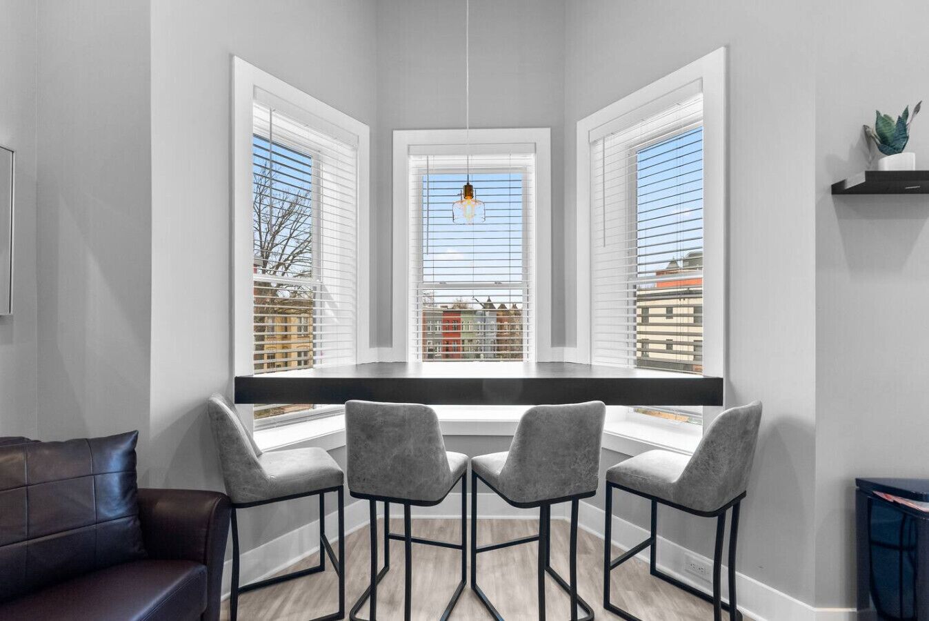 A modern kitchen with a built-in window seat, three grey chairs, and a hanging light fixture.