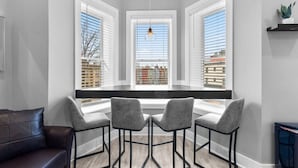 A modern kitchen with a built-in window seat, three grey chairs, and a hanging light fixture.