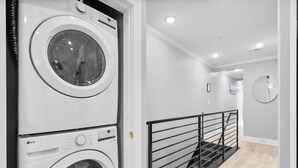 A laundry room with stacked washing machines and a staircase with a metal railing.