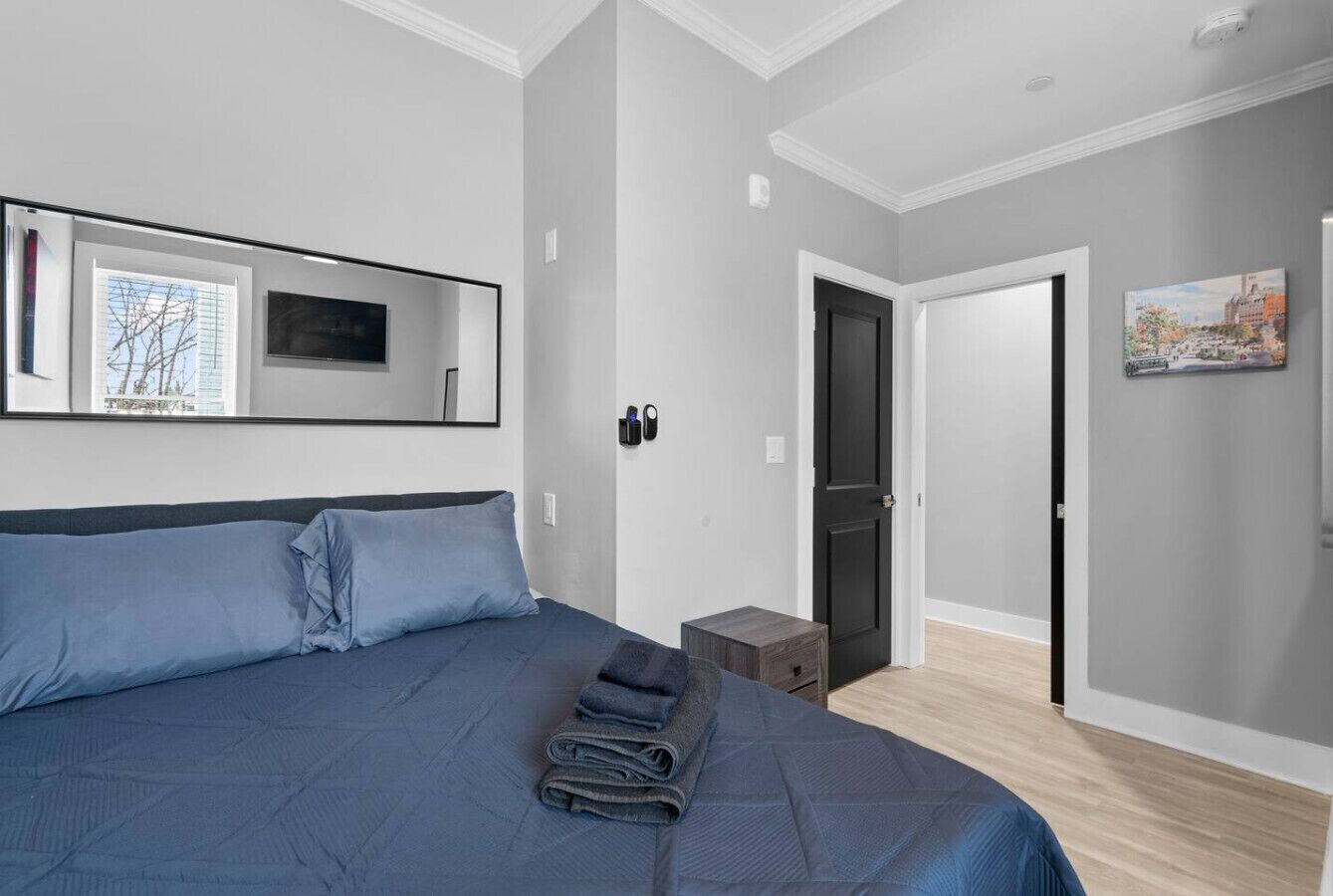 A bedroom with a large bed, a flat-screen TV mounted on the wall, and a door leading to another room.