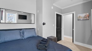 A bedroom with a large bed, a flat-screen TV mounted on the wall, and a door leading to another room.