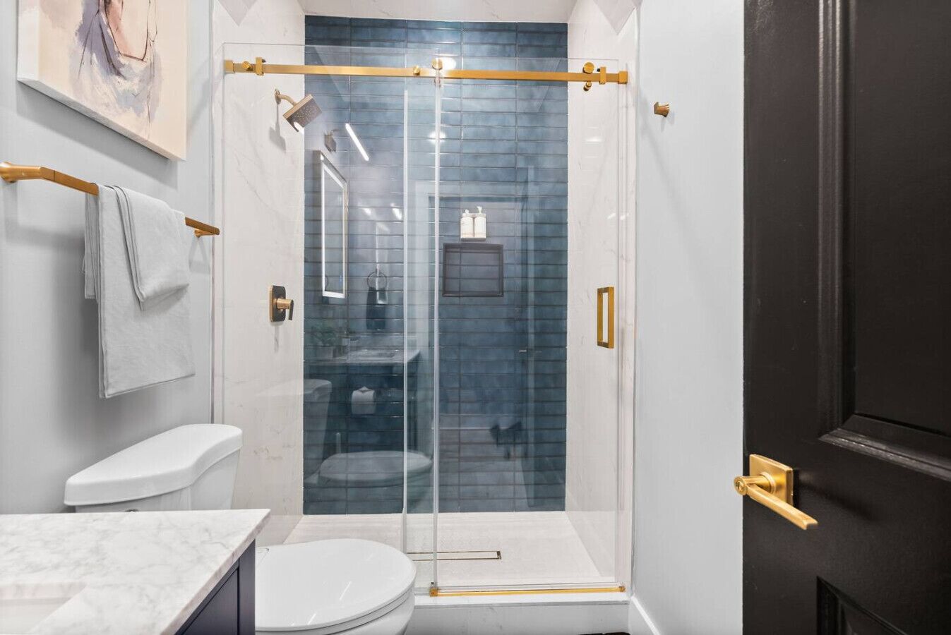 Een moderne badkamer met een douchecabine van glas, een wit toilet en een marmeren aanrechtblad.