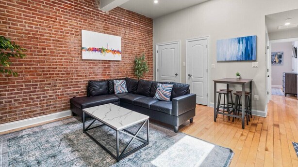 A modern living room with a brick wall, a sectional sofa, a coffee table, and a dining area with stools.