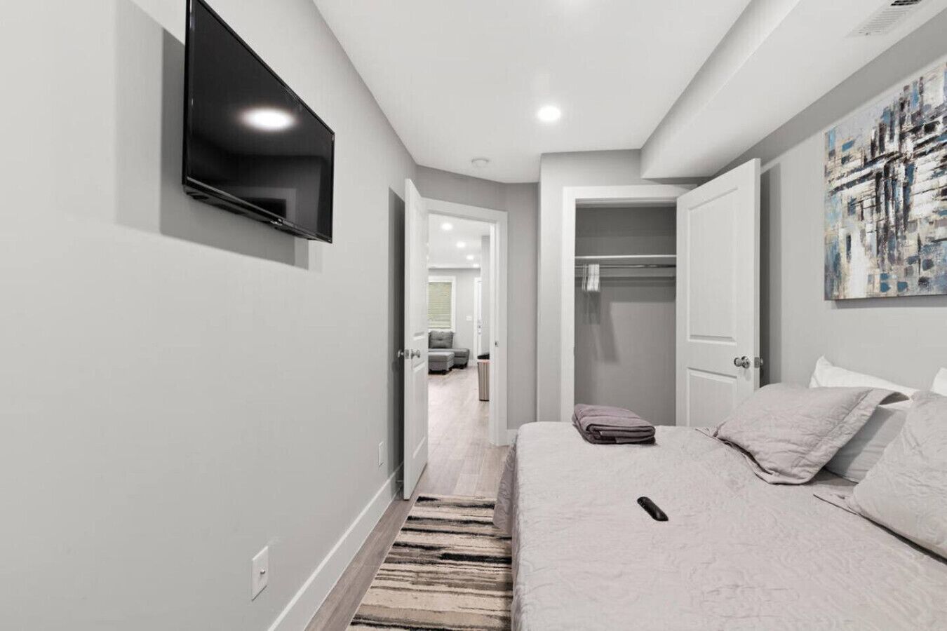 A modern bedroom with a bed, a flat-screen TV mounted on the wall, and a walk-in closet.