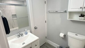 Un baño moderno con tocador blanco, un espejo, un inodoro y una zona de ducha.