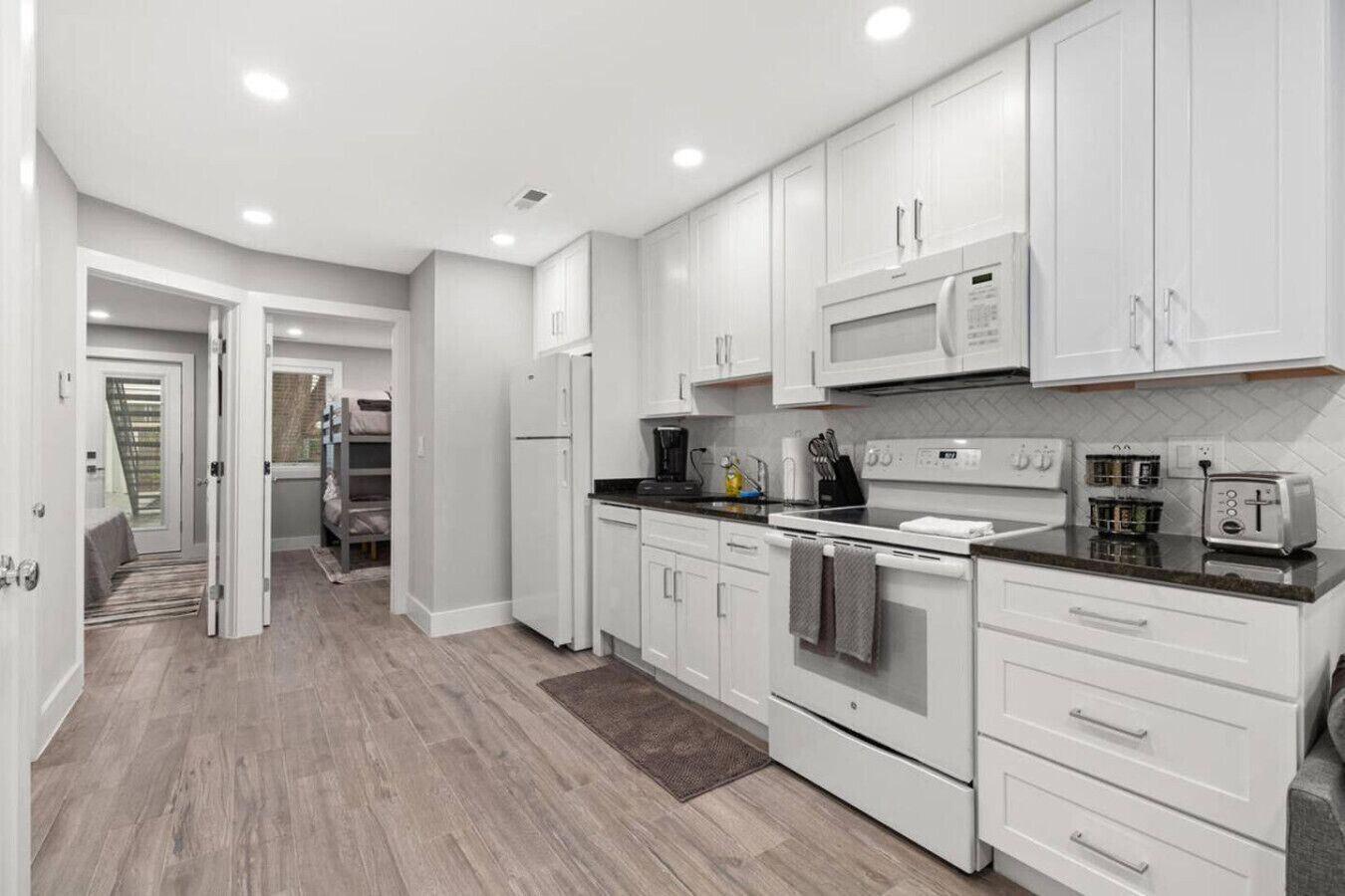 A modern kitchen with white cabinetry, a stainless steel refrigerator, a microwave, a stove, and a toaster.