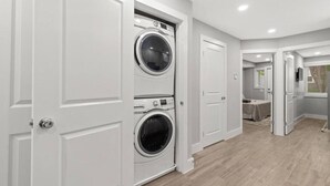 Un lavadero con dos lavadoras y secadoras apiladas de carga frontal, armarios blancos y piso de madera.