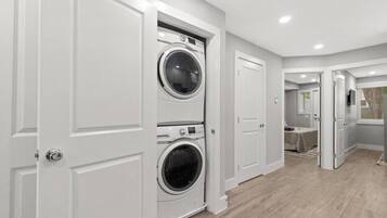 A laundry room with two stacked front-loading washers and dryers, white cabinetry, and a wooden floor.