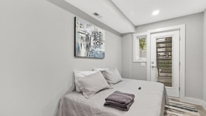 Un dormitorio moderno con una cama grande, un cuadro y un ventanal corredera que da a un balcón.