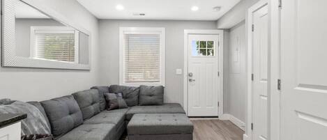 A modern living room with a sectional sofa, a small ottoman, and a patterned rug.