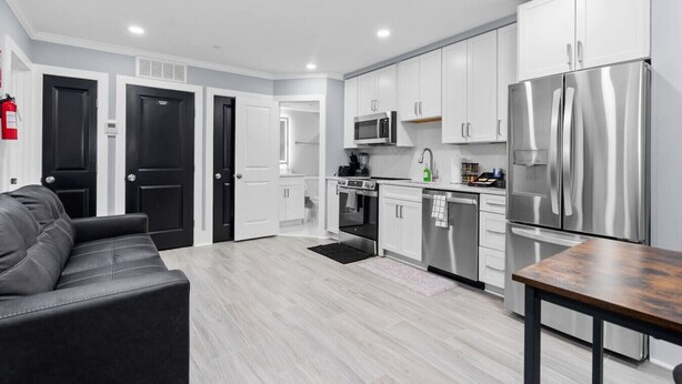 A modern kitchen with white cabinets, stainless steel appliances, and a grey leather sofa. - New DC Unit+Prime Location+2BR+Private Parking (Washington)