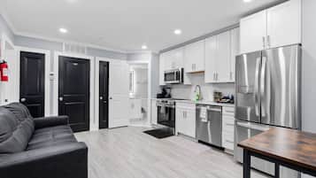 Una cocina moderna con armarios blancos, electrodomésticos de acero inoxidable y un sofá de cuero gris.